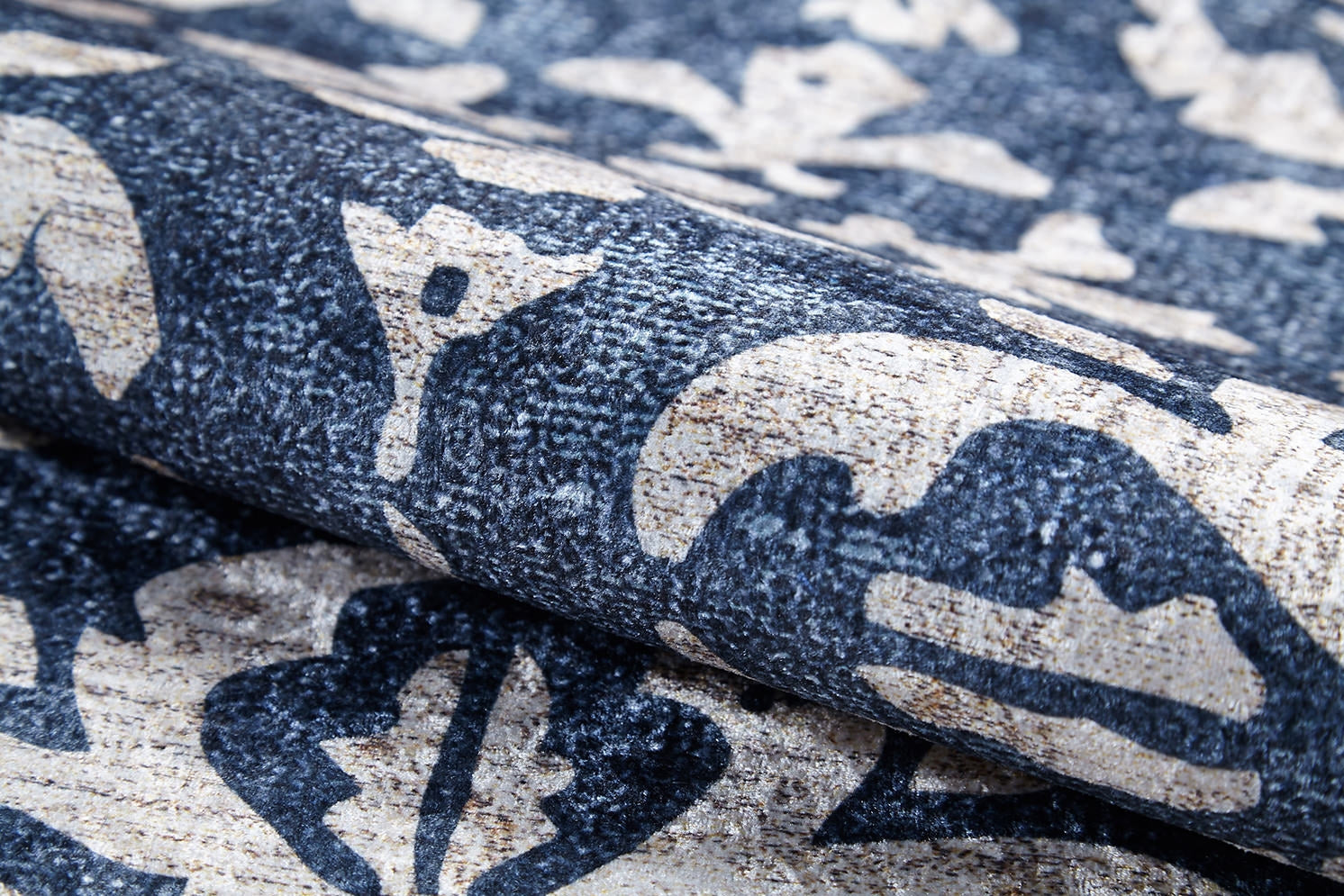 A close-up of the Antique Flourish - Washable Rug - JR1591 shows its textured surface with a bold, abstract floral and leaf pattern in dark blue and beige—perfect as a stylish, washable rug for high-traffic areas.