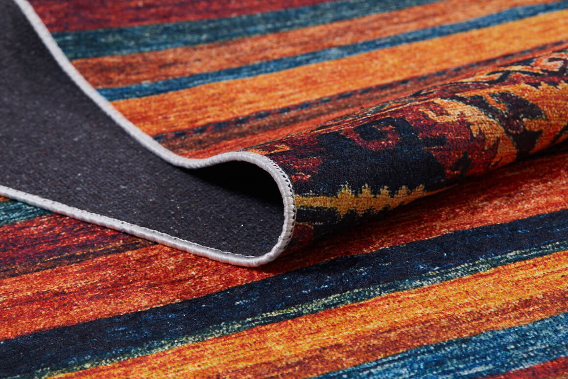 A close-up of the Arctic Chill - Washable Rug - JR860 shows bold horizontal stripes in red, orange, yellow, and blue. A folded corner reveals its dark backing and stitched edge—ideal for adding color to busy spaces.