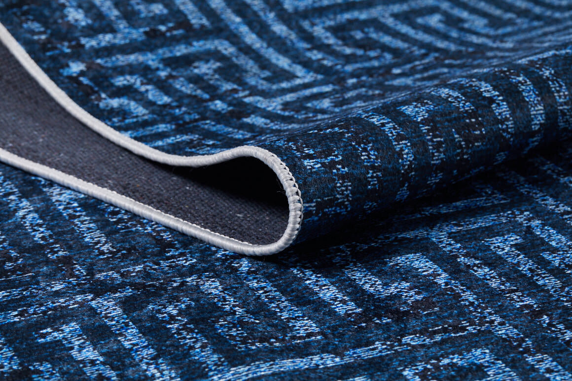 A close-up of the Art Deco Elegance - Washable Rug - JR1224 showcases its blue geometric maze-like design and stitched finished edge. The slightly curled corner highlights the rug’s texture, thickness, and suitability for high-traffic areas.