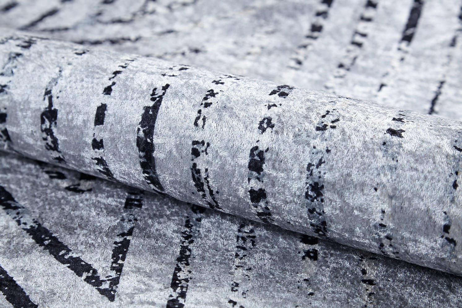 A close-up of the Art Deco Empress - Washable Rug - JR1867 in gray-anthracite, featuring black, irregular vertical lines and a soft, velvety surface. Rolled to show its flexible, plush texture—ideal for high-traffic areas.