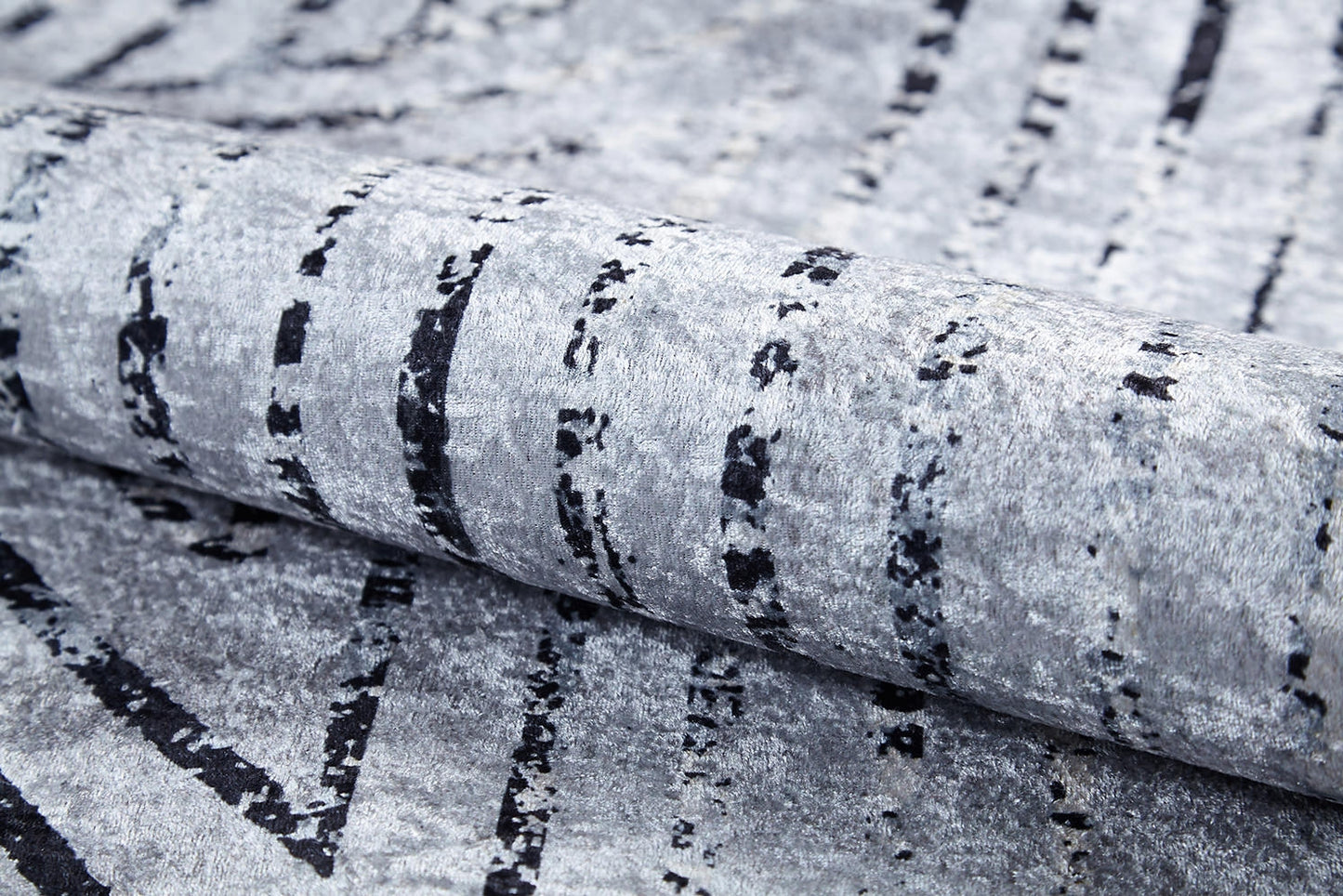 A close-up of the Art Deco Empress - Washable Rug - JR1867 in gray-anthracite, featuring black, irregular vertical lines and a soft, velvety surface. Rolled to show its flexible, plush texture—ideal for high-traffic areas.