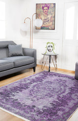 A modern living room with a gray sofa, the Artisan Tapestry - Washable Rug - JR176 (purple patterned, ideal for high-traffic areas), a side table with a vase, framed tattooed art, and two white globe lamps behind the sofa.