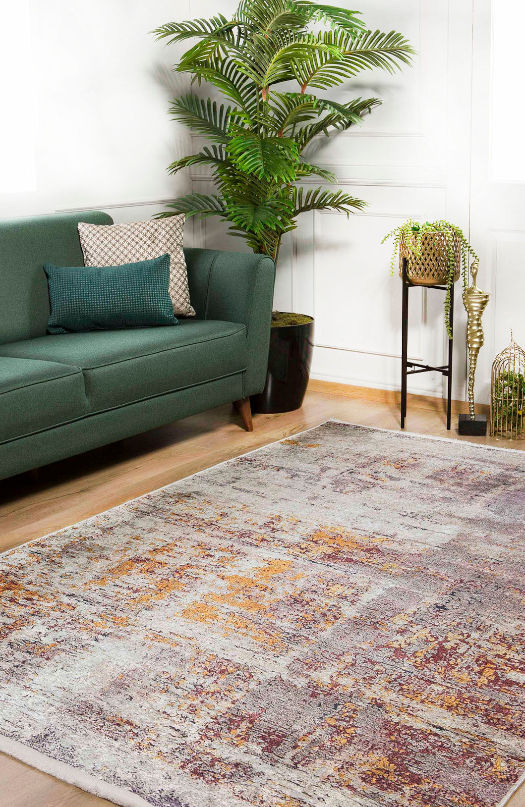 A modern living room featuring a green sofa with decorative pillows, a large leafy plant, small table with potted plants, and the Artistic Abstraction - Washable Rug - JR775 in shades of gray, yellow, and burgundy on a wooden floor.