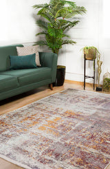 A modern living room featuring a green sofa with decorative pillows, a large leafy plant, small table with potted plants, and the Artistic Abstraction - Washable Rug - JR775 in shades of gray, yellow, and burgundy on a wooden floor.
