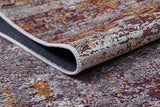 A close-up of the Artistic Abstraction - Washable Rug - JR775 with a folded corner highlights its textured flat weave and stitched edge. The design displays shades of gray, yellow, and burgundy.