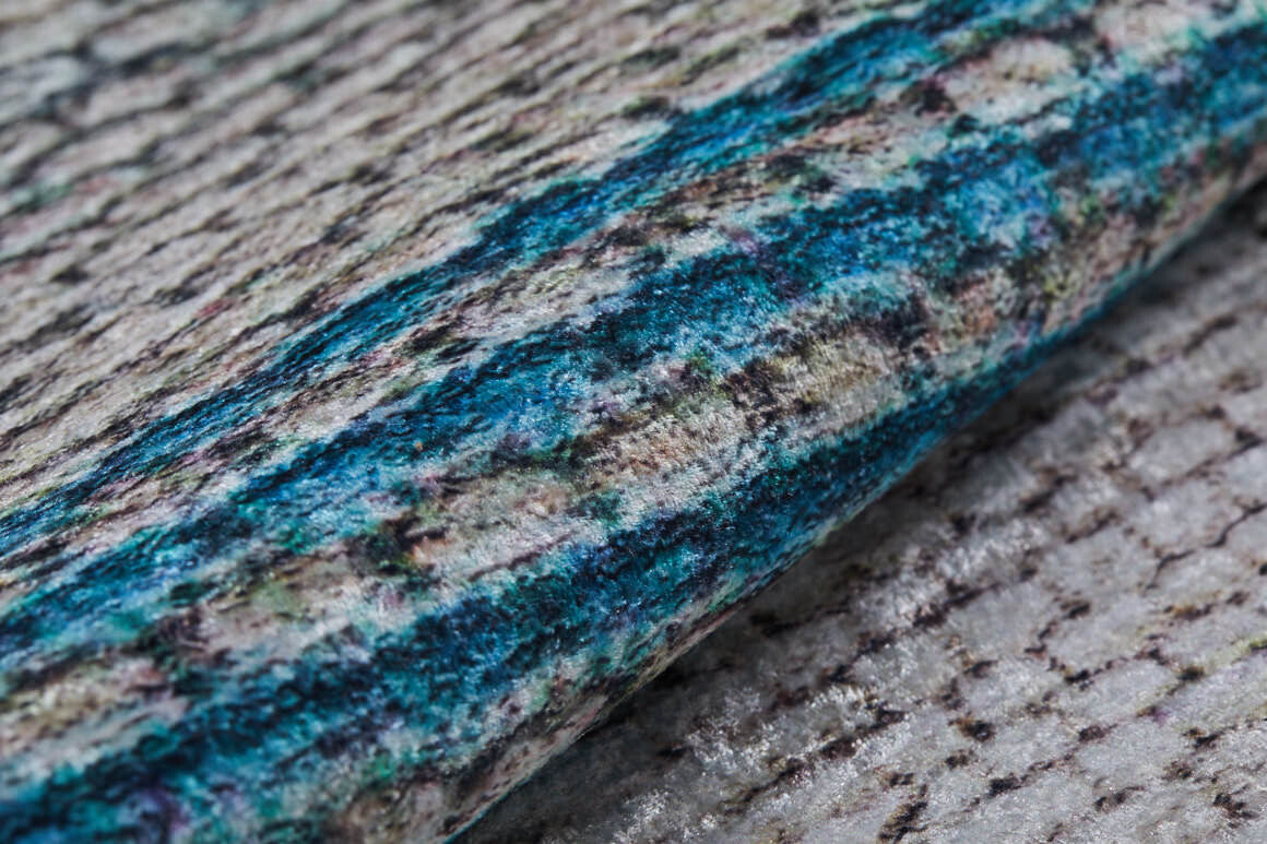 A close-up of the Artistic Angles - Washable Rug - JR908, showcasing its rolled-up blue surface with gray and beige tones and a woven texture—perfect for high-traffic areas.