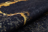 A close-up of the Azure Glow - Washable Rug - JR1337 shows its black base with gold textured fabric, ornate metallic-accented patterns, and a luxurious feel—ideal for high-traffic spaces.