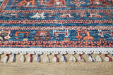 A close-up of the Berber Beauty - Washable Rug - JR5092, featuring blue with red and cream geometric patterns and colorful tassels on the edge, placed on a wooden floor—ideal for high-traffic areas.