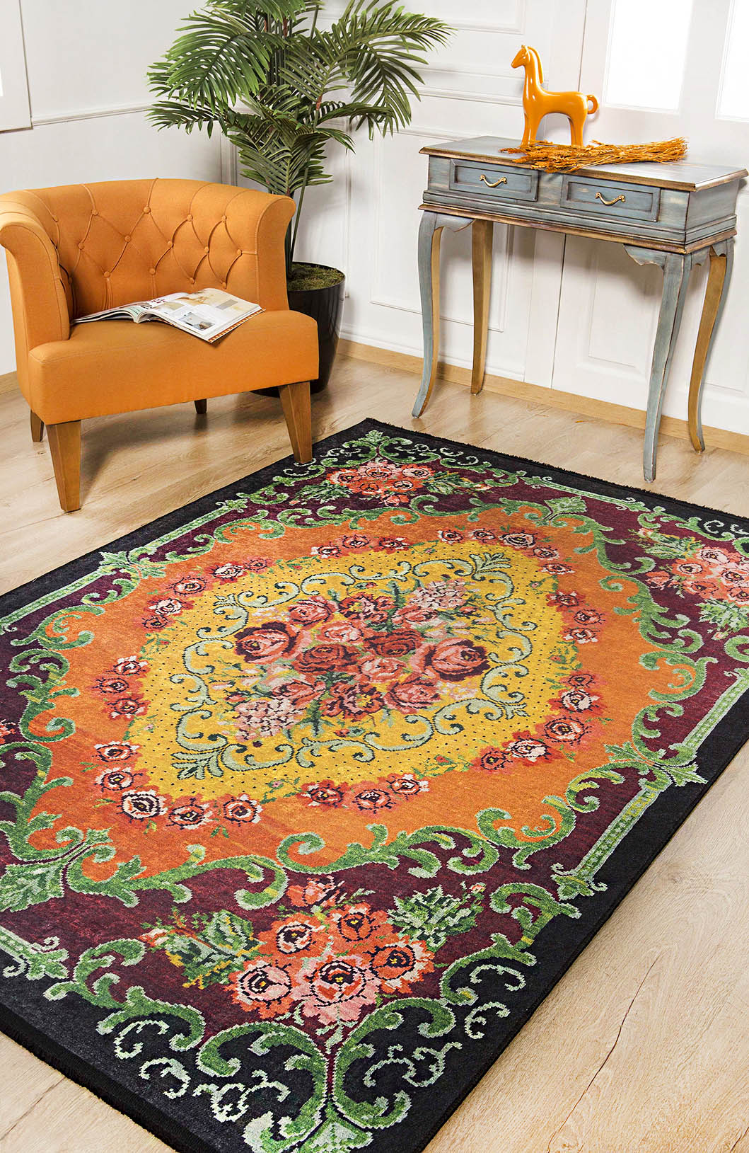 The Blossoming Garden - Washable Rug - JR150, featuring a vibrant floral pattern, lies on a light wood floor near an orange armchair, a small blue table with a horse figurine, and lush green plant against white paneled walls.