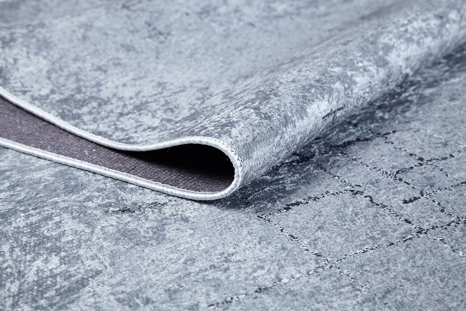 A close-up of the Bohemian Driftwood - Washable Rug - JR1951 in gray-anthracite shows its soft top, grid-patterned non-slip backing, and slightly raised edge—ideal for high-traffic areas and easy cleaning.