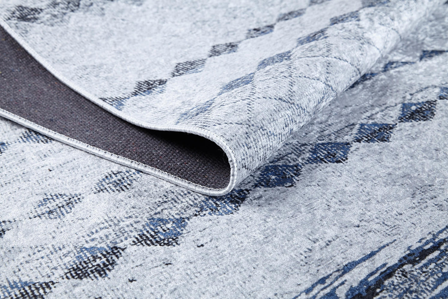 A close-up of the Bohemian Reverie - Washable Rug - JR1974 (Outlet) US shows its light gray and blue pattern, a folded corner revealing the dark, textured backing and detailed weave—ideal for high-traffic areas.