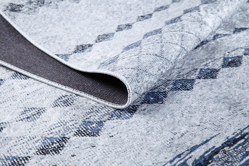 Load image 1 in gallery view. A close-up of the Bohemian Reverie - Washable Rug - JR1974 (Outlet) US shows its light gray and blue pattern, a folded corner revealing the dark, textured backing and detailed weave—ideal for high-traffic areas.