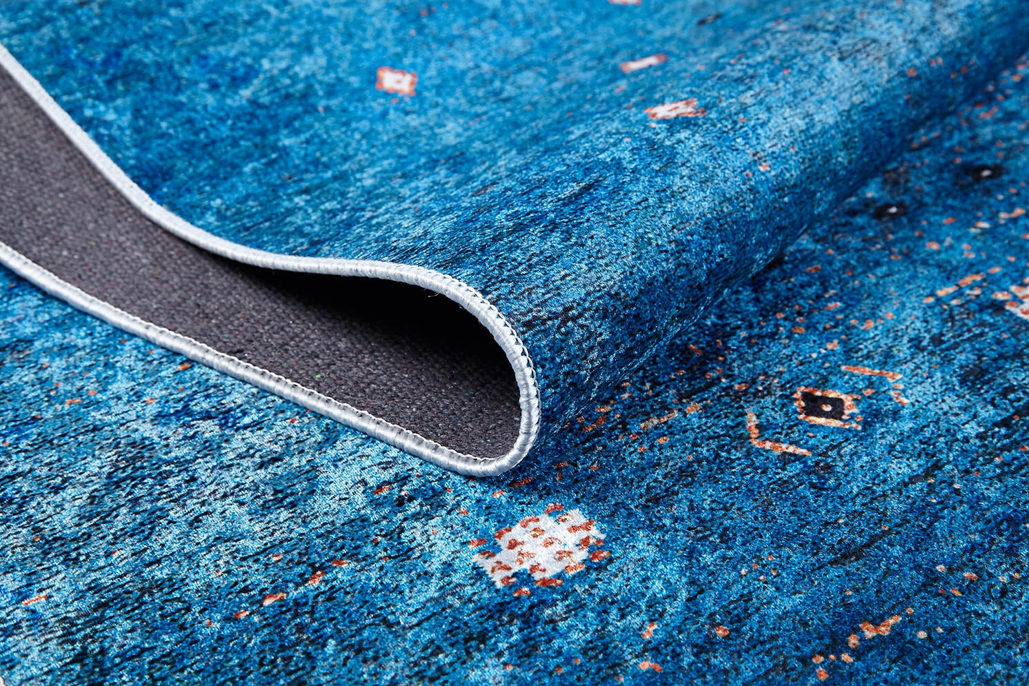 A close-up of the Bohemian Whirlwind - Washable Rug - JR1989 in blue, featuring small geometric designs and a textured gray underside—ideal for high-traffic areas, easy to maintain, and finished with neatly stitched edges.