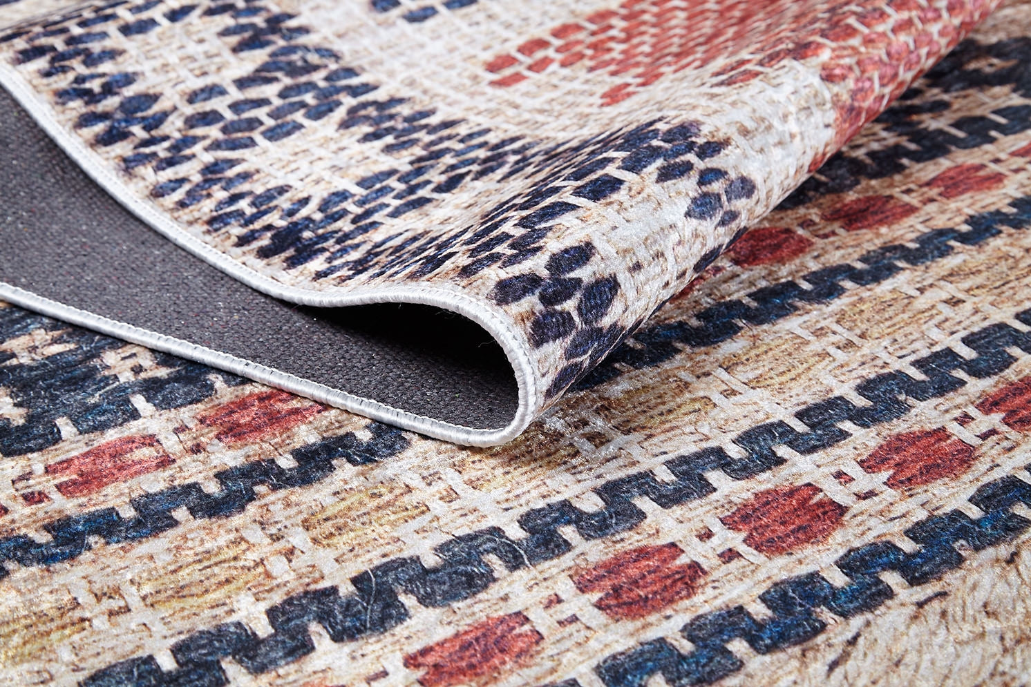 A close-up of the Boho Bliss - Washable Rug - JR1723 showcases red, blue, and beige geometric patterns. A folded corner reveals the dark backing and stitched edge—ideal for fans of cream and beige rugs.