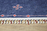 A close-up of the Boho Chic Tapestry - Washable Rug - JR5083, featuring blue with red and white geometric patterns and fringes woven with red and blue threads, displayed on a light wooden floor.