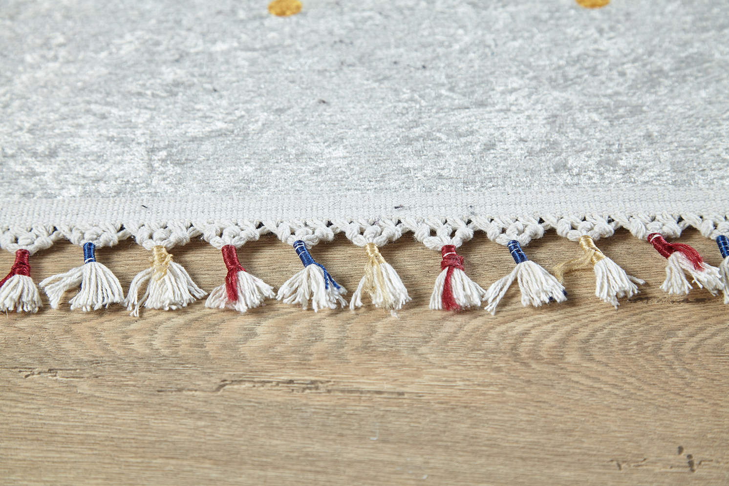 Close-up of the Boho Chic - Washable Rug - JR5103 in light gray with white, red, blue, and beige tasseled fringe, placed on a wooden floor—perfect for high-traffic areas and easy to clean.