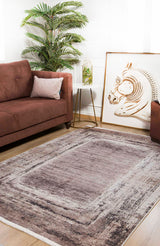 A cozy living room with a brown sofa, the Borderline Chic - Washable Rug - JR1156 in beige, bronze, and brown for high-traffic areas, a potted palm, a small white side table, and large zebra artwork resting on the floor against the wall.