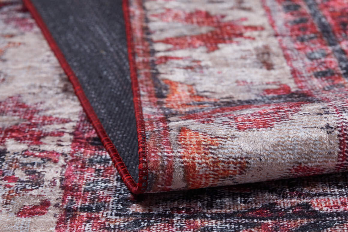 A close-up of the Classic Revival - Washable Rug - JR1374 in red, beige, and orange showcases its textured surface and flipped corner revealing the dark, non-slip backing—perfect for high-traffic areas.