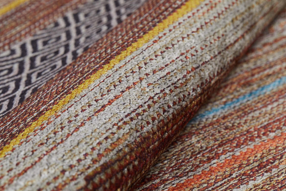 A close-up of the Coastal Breeze - Washable Rug - JR1549 shows textured woven fabric with horizontal stripes in earthy browns, orange, yellow, and cream, plus a section of black and white geometric diamond patterns.