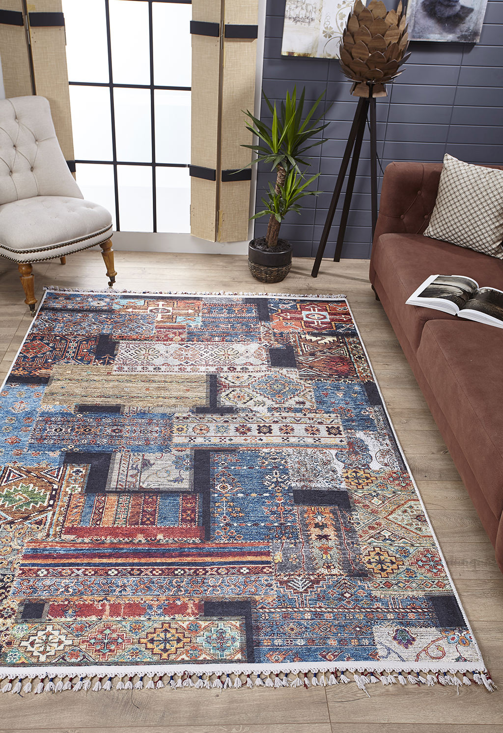 The Colorful Composition - Washable Rug - JR5107, with geometric and floral patterns, brightens a modern living room furnished with a brown sofa, light armchair, potted plant, and large windows draped in beige curtains.