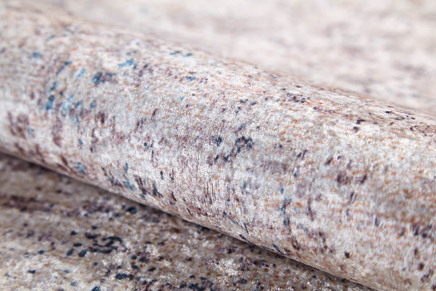 A close-up of the Copper Glow - Washable Rug - JR1700, partially unrolled to reveal its textured, plush surface with a speckled cream and beige pattern accented by blue, ideal for high-traffic areas.