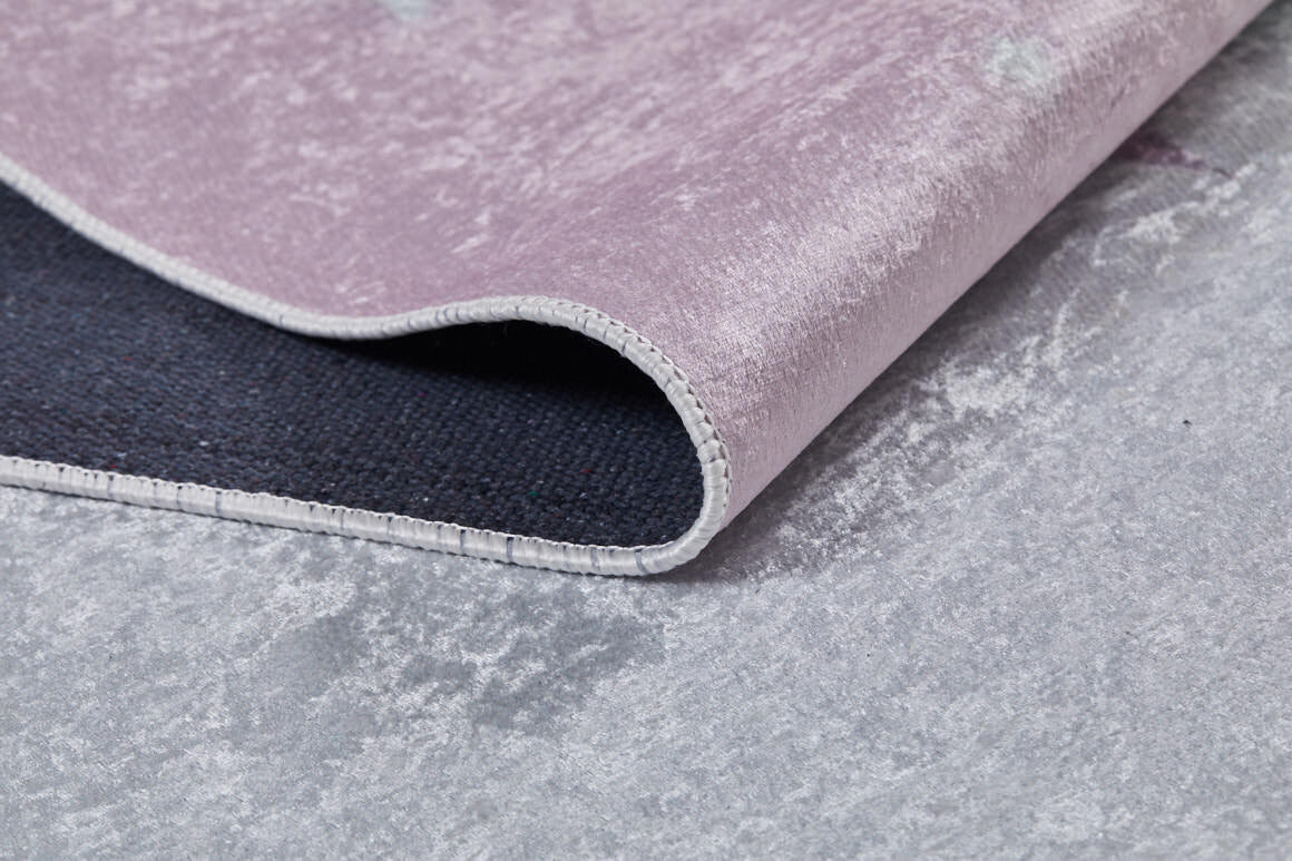 A close-up of the Cosmic Naptime - Machine-Washable Rug JRC032 featuring a soft pink flat weave, black accents, curved edge, and visible stitching, displayed on a gray textured surface.