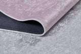 A close-up of the Cosmic Naptime - Machine-Washable Rug JRC032 featuring a soft pink flat weave, black accents, curved edge, and visible stitching, displayed on a gray textured surface.