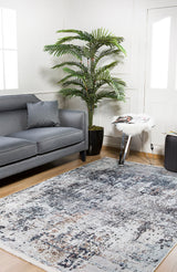 Modern living room featuring the gray sofa and a Creative Currents - Washable Rug - JR835, ideal for high-traffic areas. Natural light highlights the palm plant, crisp white walls, and a small table with magazines—perfect for everyday living.