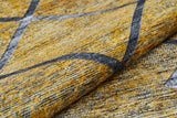 A close-up of the Crossed Connections - Washable Rug - JR1181 shows its yellow and gray geometric design with intersecting dark gray lines. Slight fabric folds highlight its texture. Ideal for high-traffic areas and easy to clean.