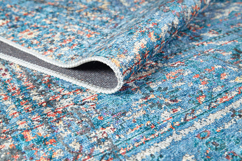 Load image 1 in gallery view. A close-up of the Desert Diamond - Washable Rug - JR5071 in blue with multicolored specks, partially folded to show its textured backing and stitched edge—ideal for high-traffic areas.