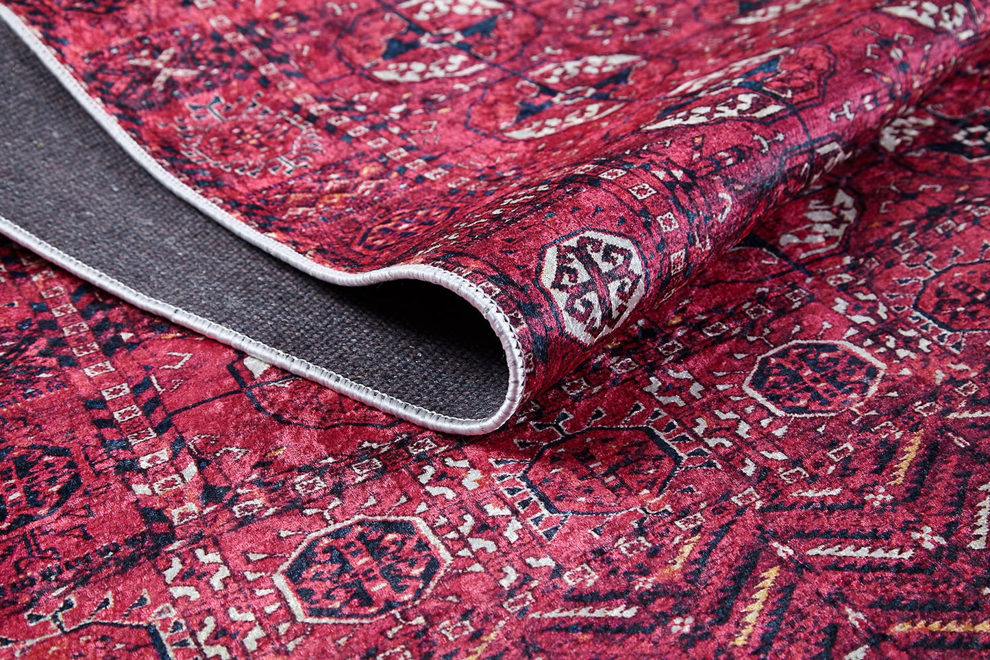 A close-up of the Desert Dreamscape - Washable Rug - JR1940 shows its red geometric pattern and durable design, with one corner lifted to reveal the dark gray underside.