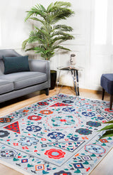 A modern living room with a gray sofa, blue ottoman, glass side table with a face vase, large green plant, and the Desert Drift - Washable Rug - JR1523—ideal for high-traffic areas—on light wood flooring.