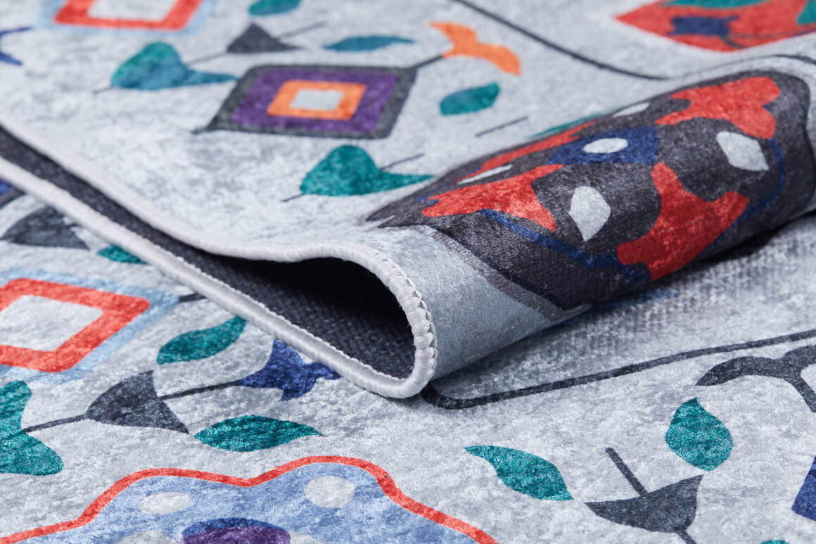 A close-up of the Desert Drift - Washable Rug - JR1523, folded to highlight its vibrant geometric and floral patterns in red, blue, green, orange, and purple on a light gray background—perfect for high-traffic areas.