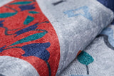 Close-up of the Desert Drift - Washable Rug - JR1523, featuring red, blue, teal, and gray abstract patterns. Its soft, plush surface is shown gently folded—perfect for high-traffic areas and easy to wash.