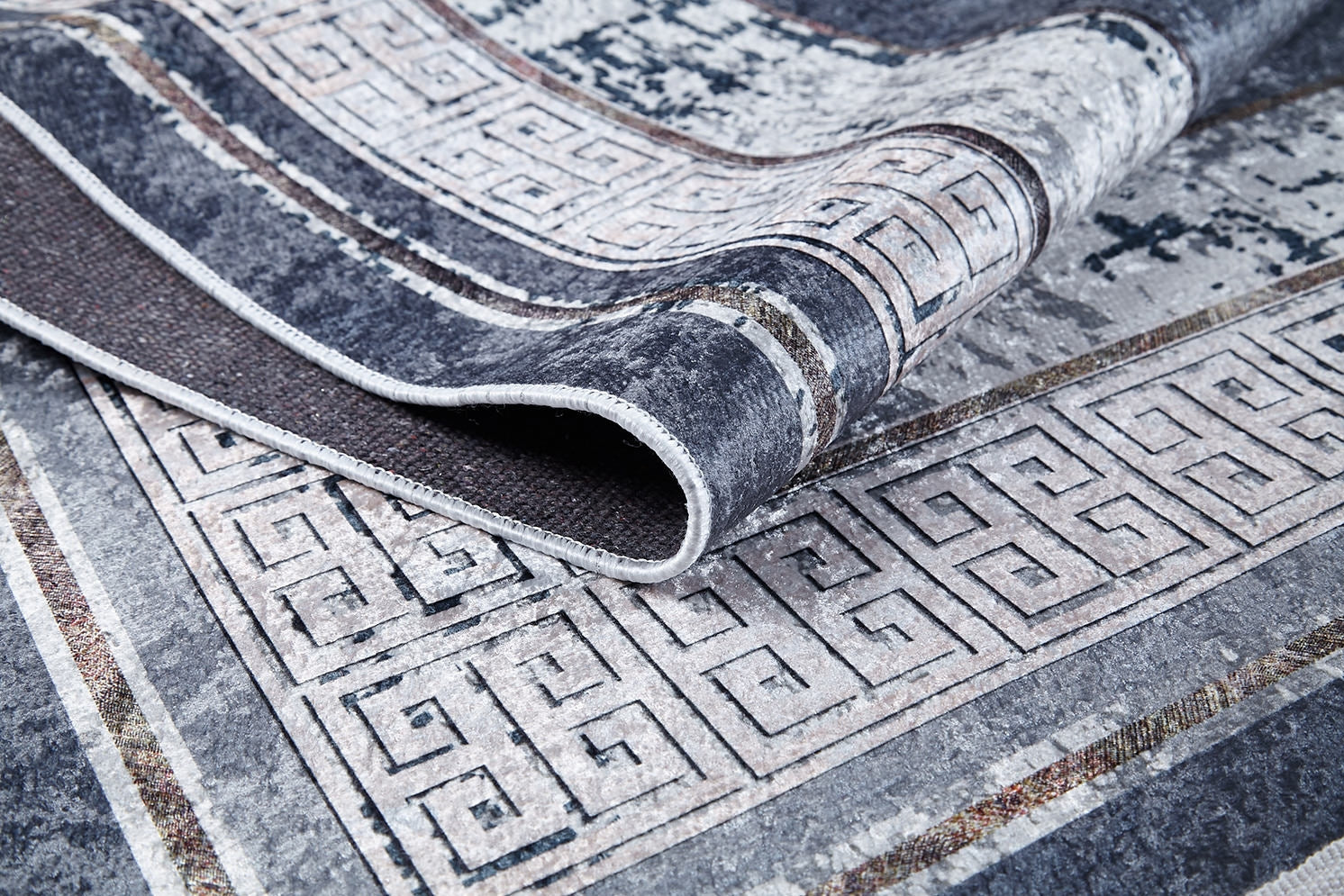 A close-up of the Dramatic Boundaries - Washable Rug - JR1810 shows its folded geometric Greek key pattern in shades of gray, white, and black—durable texture and intricate detailing make it ideal for high-traffic areas.