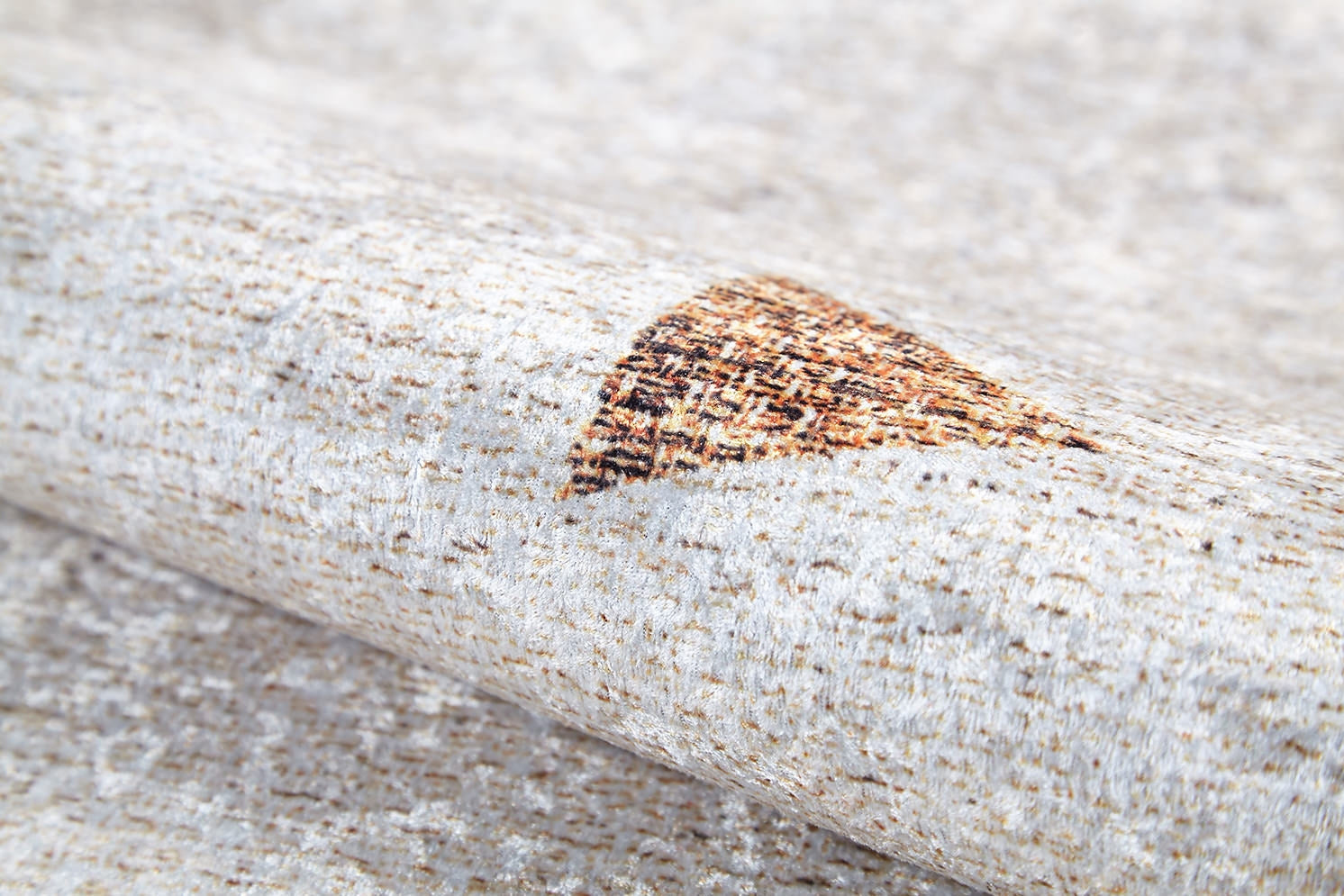 A close-up of the Ebony Ivory - Washable Rug (JR1994), rolled to reveal its beige surface with small brown and orange triangles—an ideal choice for allergy-sensitive households and busy, high-traffic areas.