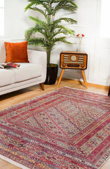 A living room featuring the Elegant Embellishments Washable Rug - JR43 in red for high-traffic areas, a white sofa with an orange cushion, a vintage radio on wooden legs, a tall potted plant, and a magazine on the sofa.