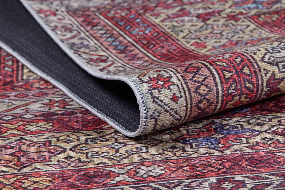 A close-up of the Elegant Embellishments - Washable Rug - JR43 showcases its red, cream, and gold geometric and floral patterns, with a folded corner revealing the black nonslip backing—ideal for high-traffic areas.