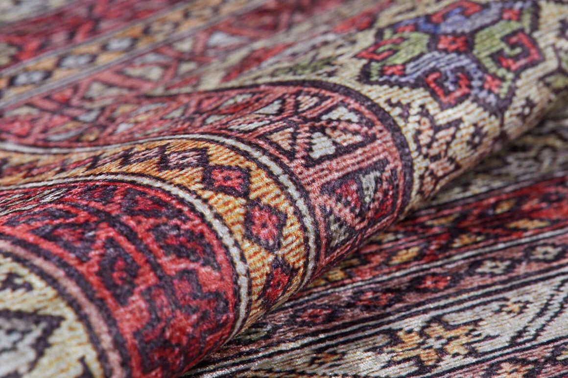 A close-up of the Elegant Embellishments - Washable Rug - JR43 displays geometric patterns in red, yellow, green, black, and beige. Slightly folded to reveal its texture, this rug is ideal for high-traffic areas and easy to clean.