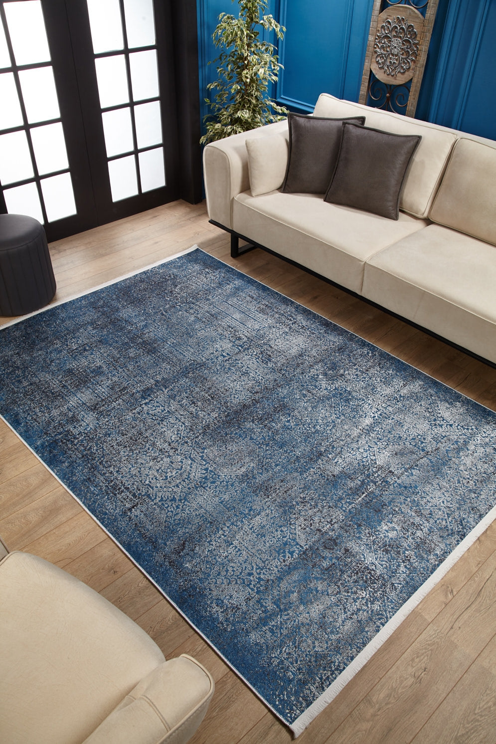 A modern living room with beige sofas, dark accent pillows, a green potted plant, blue walls with molding, black-and-white French doors, wooden flooring, and the Elegant Vine - Washable Rug - JR1847.
