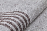 Close-up of Elegant and Chic - Washable Rug - JR1509: a light gray, textured surface with dark wavy lines. Slightly rolled, it offers a soft, fabric-like feel and durability perfect for high-traffic areas.