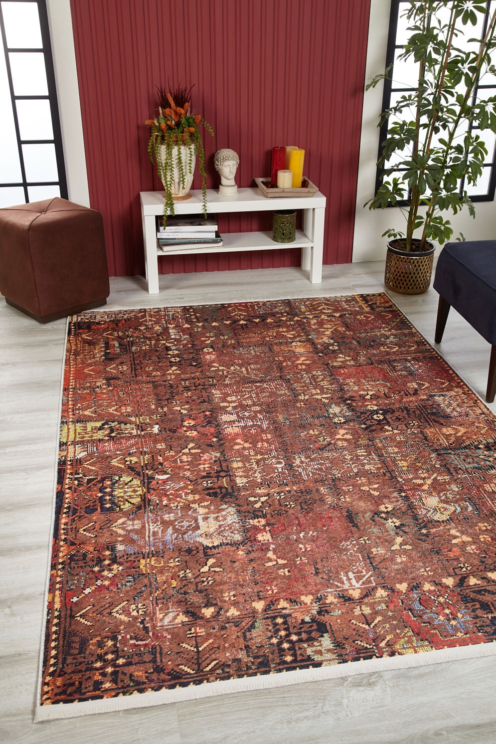 A living room with the Ethereal Elegance - Washable Rug - JR1651 (Outlet) US on light wood flooring, a white console table, plant, brown ottoman, and navy chair against a red accent wall—ideal for high-traffic areas.