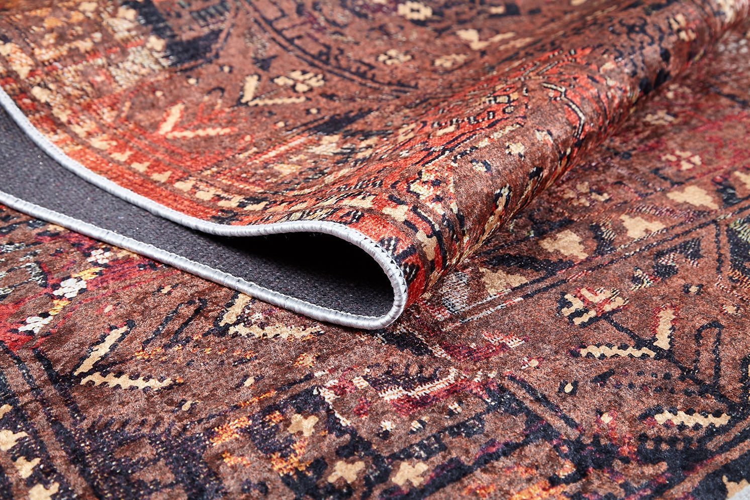 A close-up of the Ethereal Elegance - Washable Rug - JR1651 (Outlet) US shows its intricate bronze and brown design, partially folded to display the textured dark gray underside—ideal for high-traffic areas.