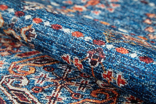 Load image 1 in gallery view. A close-up of the Ethereal Essence - Washable Rug - JR5087 in blue displays its intricate orange, white, and red geometric and floral patterns, highlighting the texture and flat weave as the rug is partially folded.