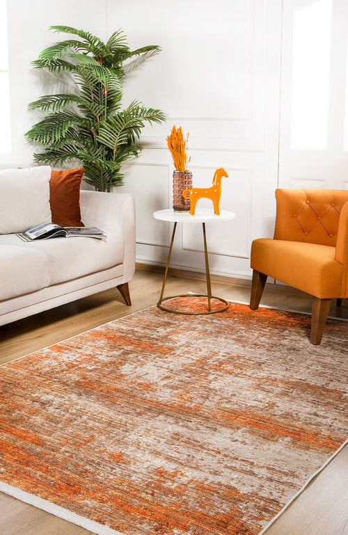 Load image 1 in gallery view. A modern living room with a beige sofa, orange chair, round white table displaying a vase of orange flowers and a decorative horse. The floor features the Fluffy Brushed - Washable Rug - JR584 in orange, with a tall plant in the corner.