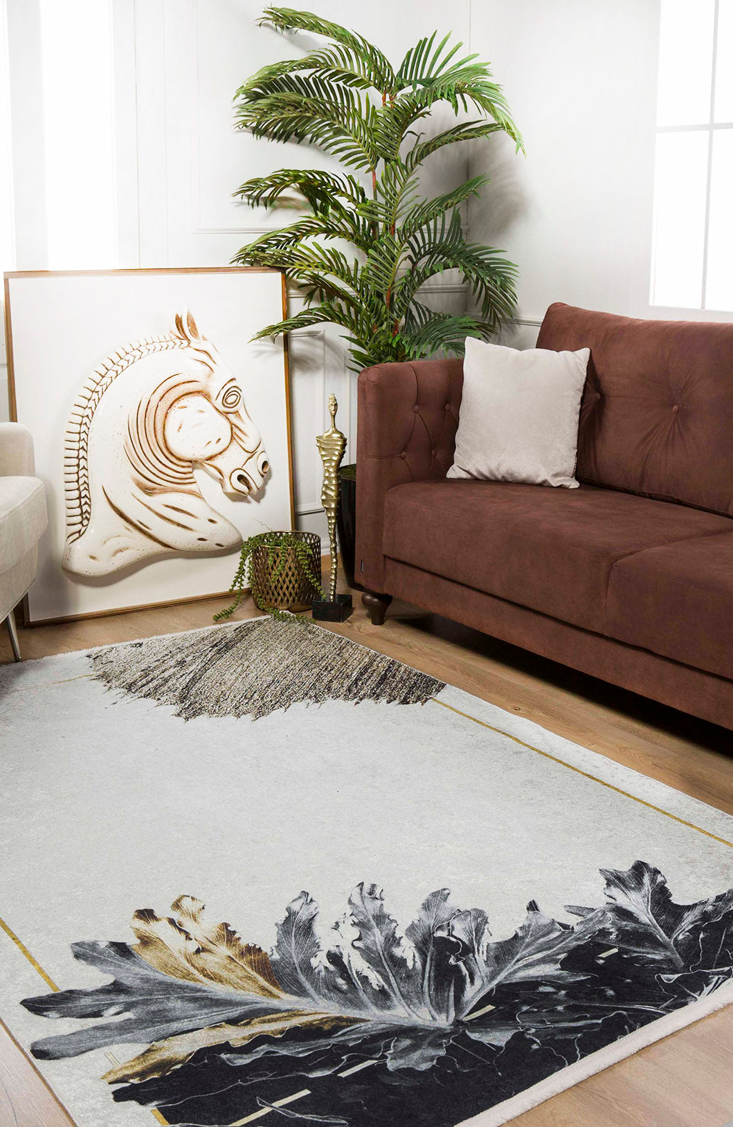 A modern living room features a brown sofa, white pillow, green potted plant, framed horse artwork, and the Funky Floral Frenzy - Machine-Washable Rug JR1376 in cream and beige abstract leaves—ideal for high-traffic spaces.