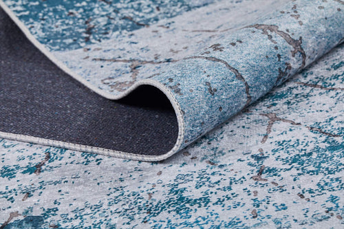 Load image 1 in gallery view. A close-up of the Geometric Glimmers - Washable Rug - JR1423 shows its blue and gray marbled pattern, a folded corner revealing the dark underside and stitched edges—ideal for high-traffic areas.