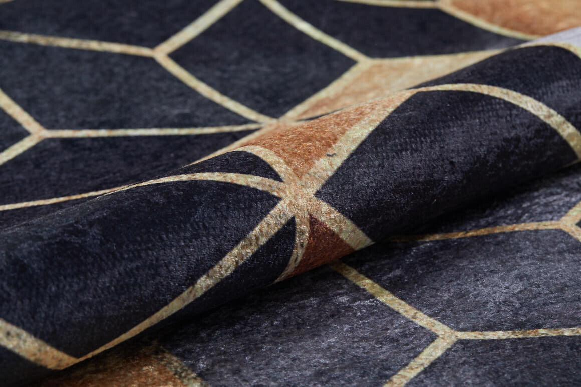 A close-up of Geometric Harmony - Washable Rug - JR1271 shows its textured fabric with a modern black, brown, and beige geometric pattern of intersecting lines forming irregular polygons. The washable rug is slightly folded.
