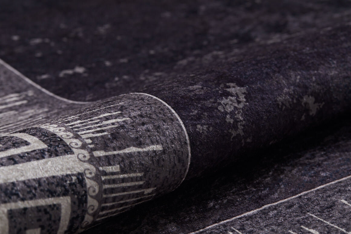 A close-up of the Geometric and Chic - Washable Rug - JR1273, partially rolled up to show its dark, textured surface with gray tones and intricate linear patterns—perfect for high-traffic areas.
