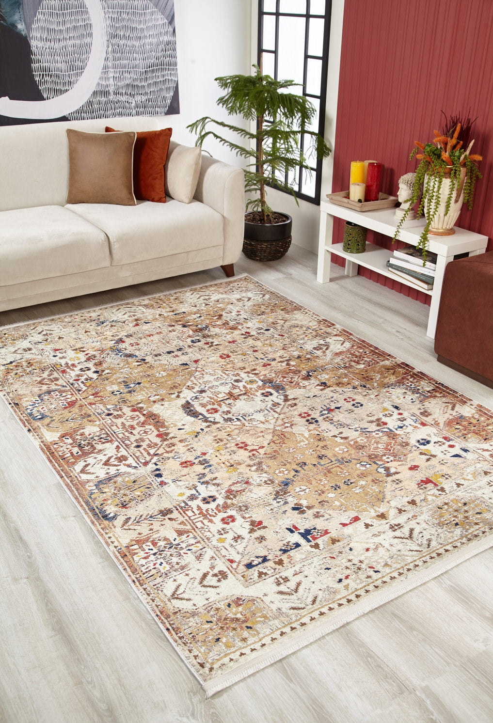 A cozy living room with a beige sofa, decorative cushions, potted plant, and the Global Getaway - Washable Rug - JR1667 featuring tan, red, and blue accents—perfect for high-traffic areas. A white table with plants stands by a bold red accent wall.